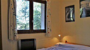 Ein Schlafzimmer mit einem Bett, einem Fenster mit Vorhängen, einem Heizkörper und einer Wandlampe.
