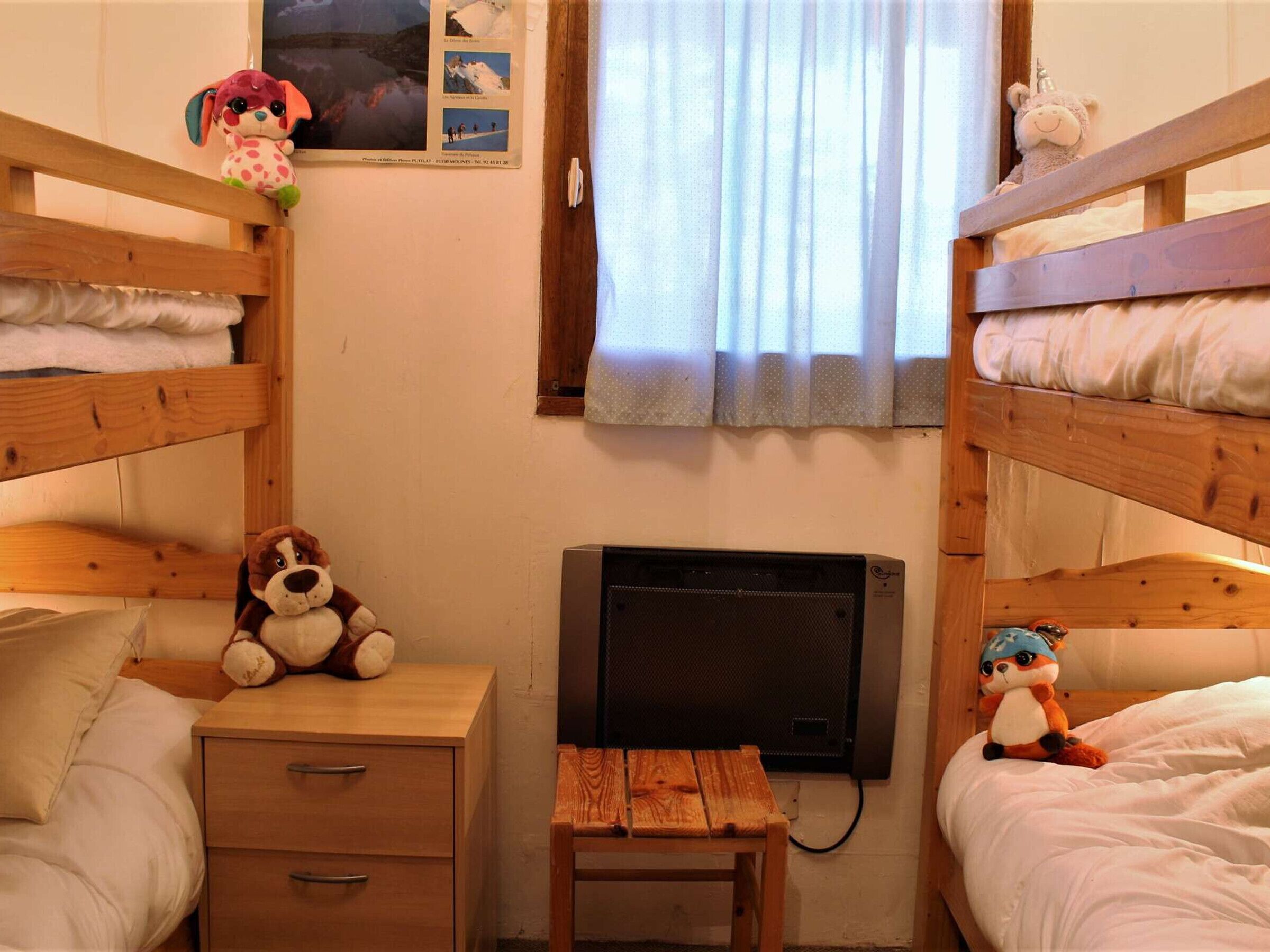 A dormitory room with bunk beds, a small wooden desk, a chair, and a heater.