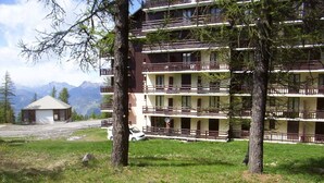 Ein mehrstöckiges Gebäude mit Balkonen, umgeben von Bäumen und mit Blick auf ein Gebirge.