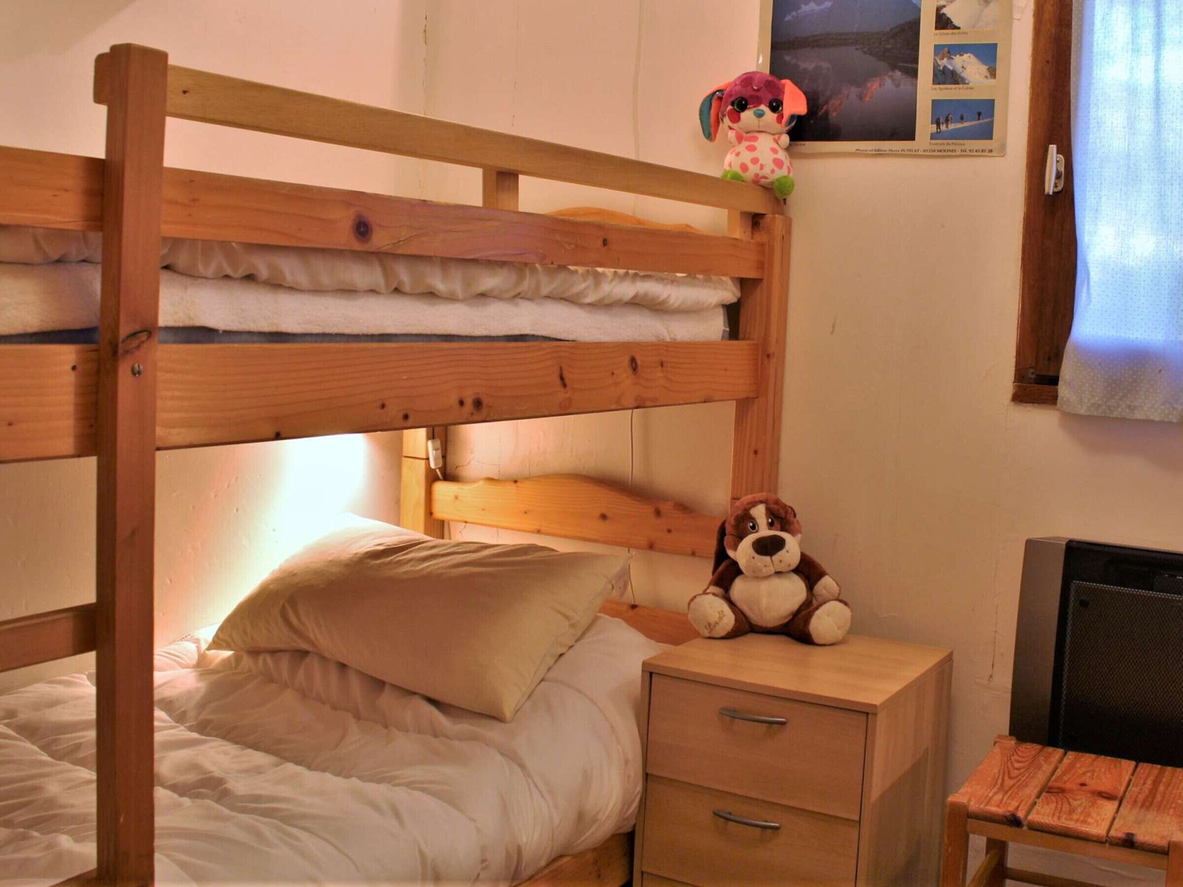 Letto a castello con struttura in legno, un comodino con cassetti, un peluche e un poster appeso al muro.