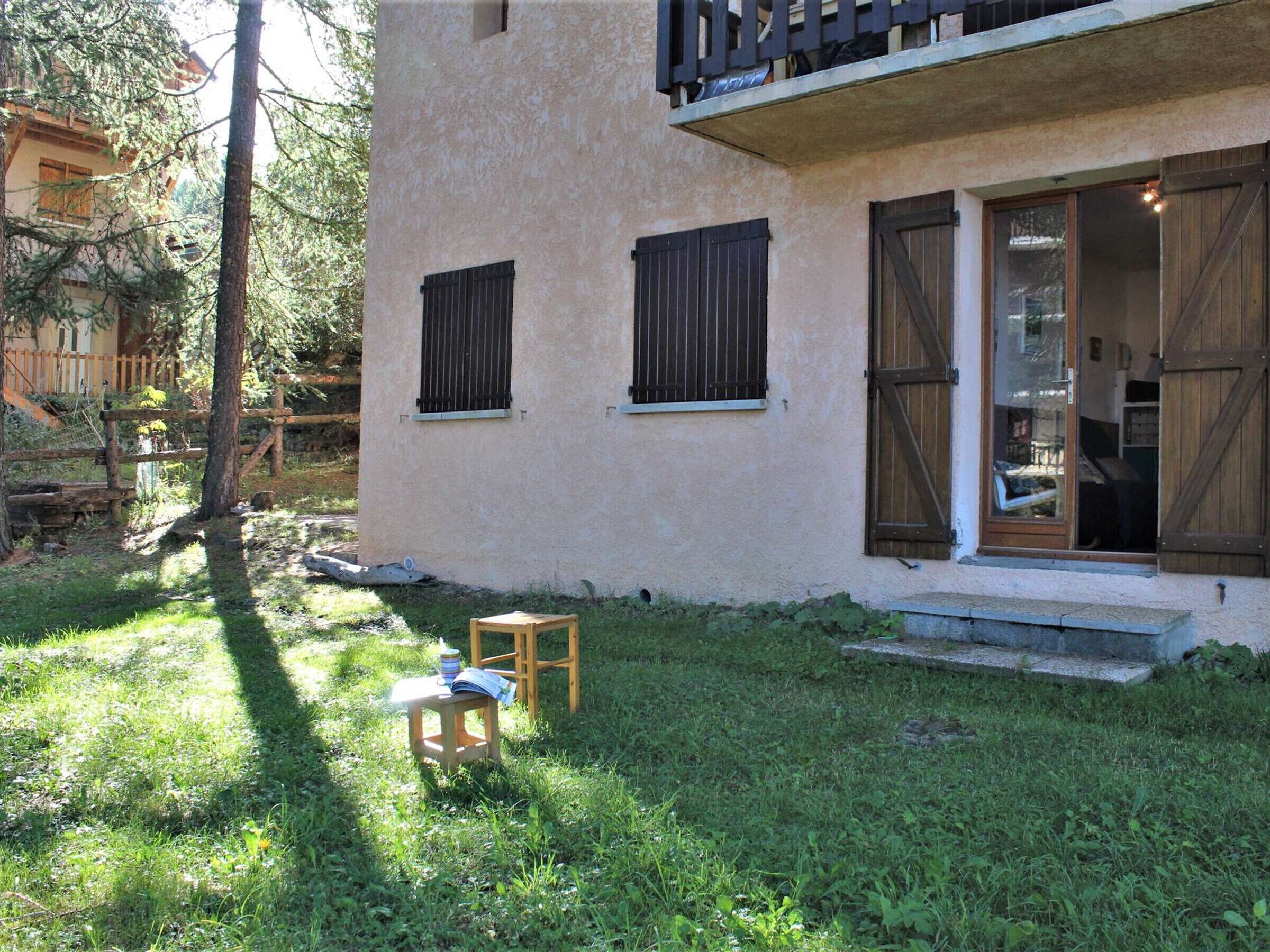 A house with a small front yard, a wooden table with a book, and a window with shutters.