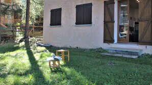 Ein Haus mit kleinem Vorgarten, einem Holztisch mit einem Buch und einem Fenster mit Fensterläden.