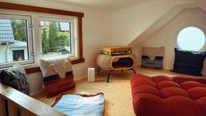 Ett mysigt rum på vinden med en röd soffa, en flätstol och ett fönster med utsikt över en trädgård.
