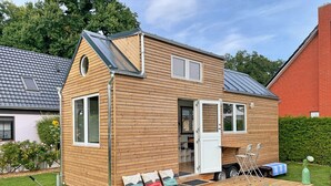 Ett litet trähus med ett sluttande tak, en ytterdörr och en liten veranda med en bänk och ett bord.