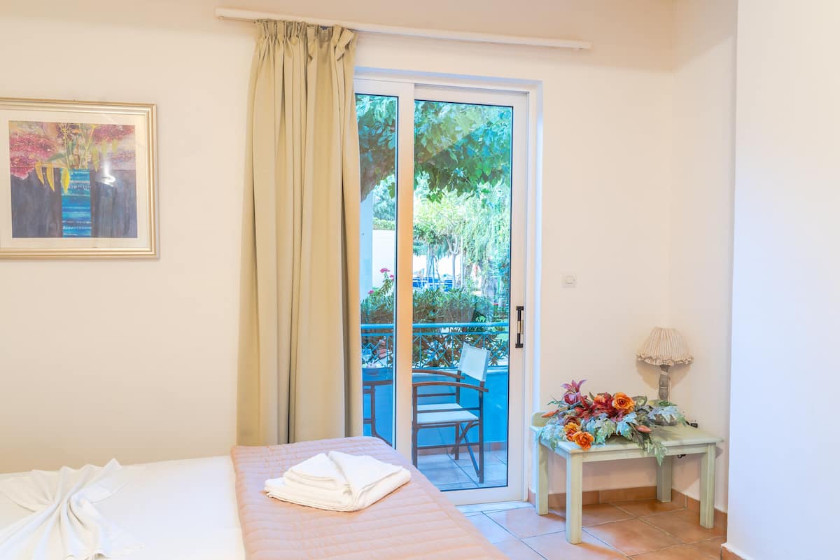 A hotel room with a bed, a framed picture, a table with flowers, and a sliding glass door to an outdoor area.
