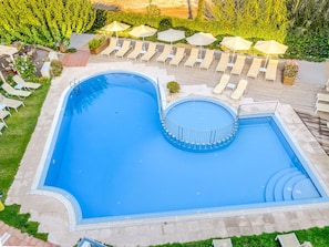 A large, rectangular swimming pool with a circular hot tub, surrounded by lounge chairs and umbrellas.