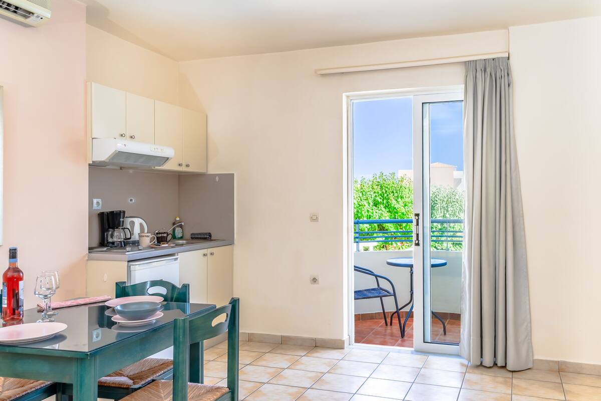 A compact kitchen with a dining area, a balcony with a table and chairs, and a sliding glass door leading to an outdoor area.