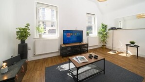 A modern living room with a flat-screen TV, wooden flooring, a coffee table, and potted plants.