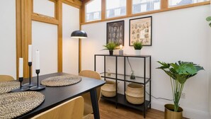 A dining area with a wooden table, black candle holders, woven placemats, and a black metal shelf with baskets and a plant.