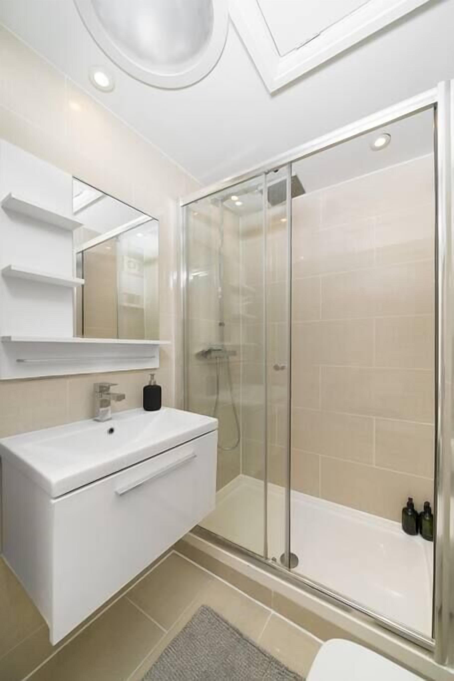 Une salle de bain moderne avec une douche à l’italienne en verre, un meuble-lavabo blanc et un miroir au-dessus du lavabo.