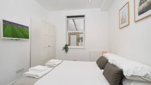 A hotel room with a bed, a TV mounted on the wall, a window, and a framed picture.