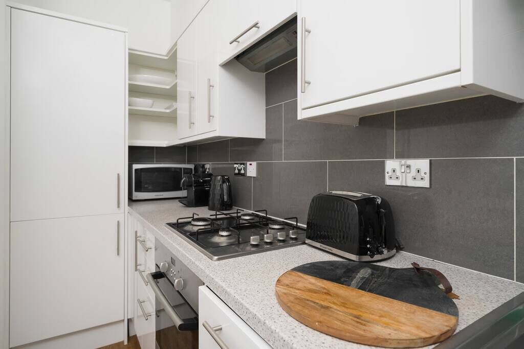 A modern kitchen with white cabinets, a gas stove, a microwave, a toaster, and a wooden cutting board on the countertop.