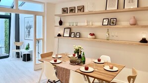 A modern dining area with a wooden table set for four, surrounded by white chairs. There are shelves above the table displaying framed artwork and decorative items. - Huge & Central 3 Bedr/4 Beds/2,5 Bath/ Covent Gdn (Greater London)