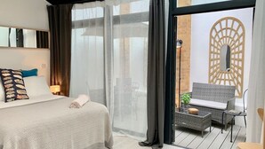 A modern hotel room with a large bed, a balcony with wicker furniture, and a view of the city. - Huge & Central 3 Bedr/4 Beds/2,5 Bath/ Covent Gdn (Greater London)