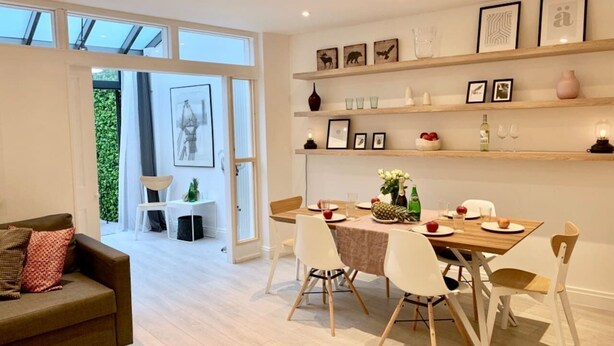 A modern living room with a sofa, dining table, and chairs. There are shelves with framed pictures and decorative items. - Huge & Central 3 Bedr/4 Beds/2,5 Bath/ Covent Gdn (Greater London)