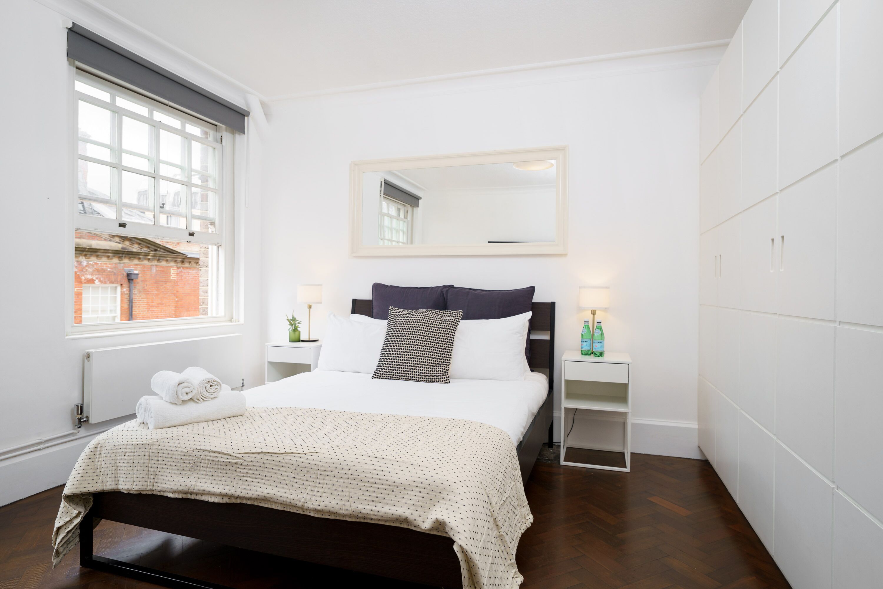 Une chambre bien rangée, avec un lit, une table de chevet, un miroir et une fenêtre.