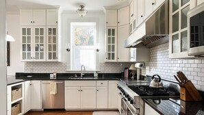 A kitchen with white cabinetry, a black countertop, a stainless steel stove, and a window with a view of trees. - Mill Haus - Heated Swimming Pool, Hot Tub, Dog Friendly, Downtown (Washington)