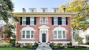 A two-story brick house with a front entrance, a covered porch, and a well-maintained garden. - Mill Haus - Heated Swimming Pool, Hot Tub, Dog Friendly, Downtown (Washington)