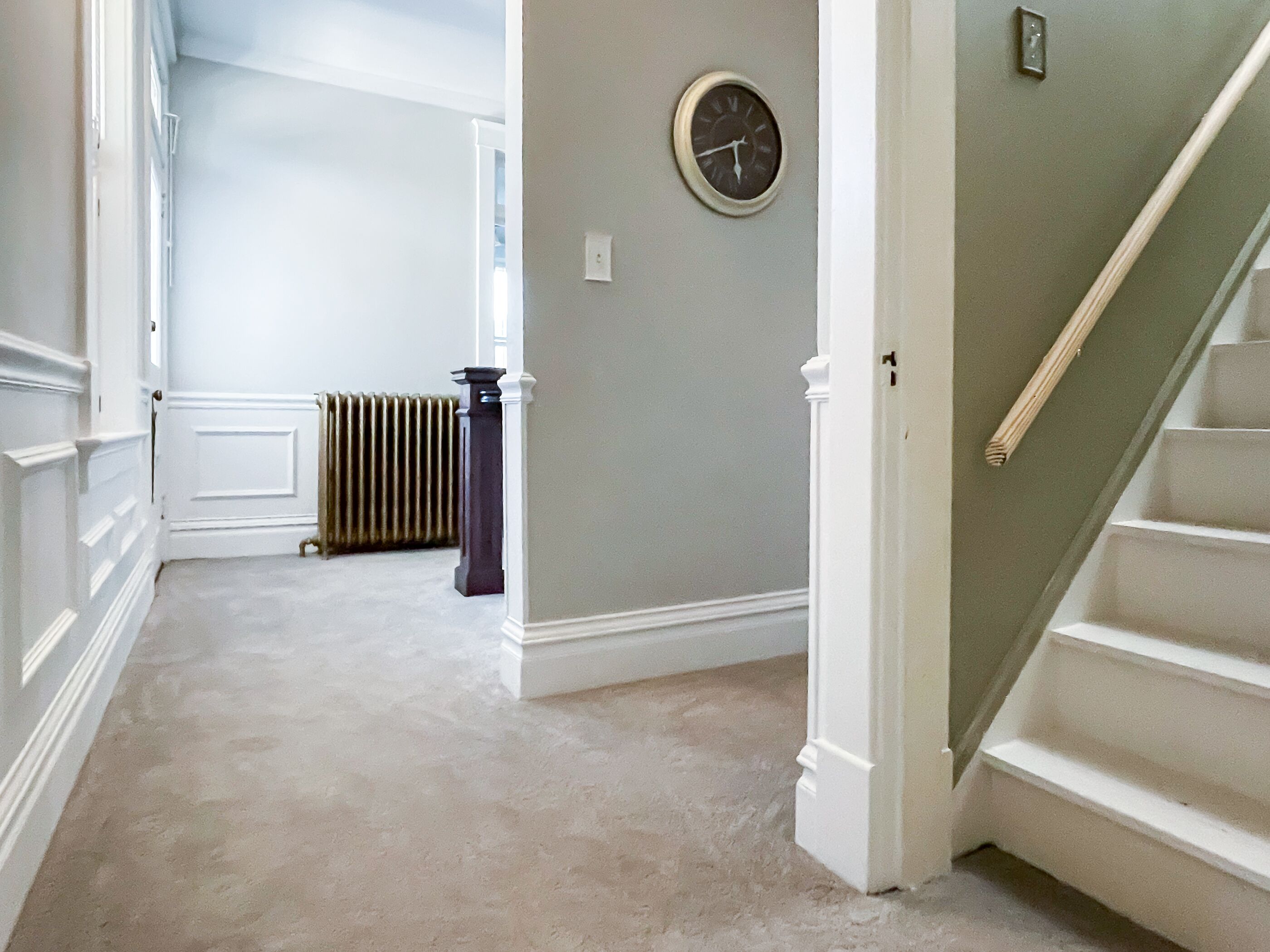 A hallway with a carpeted floor, a radiator, and a clock on the wall.