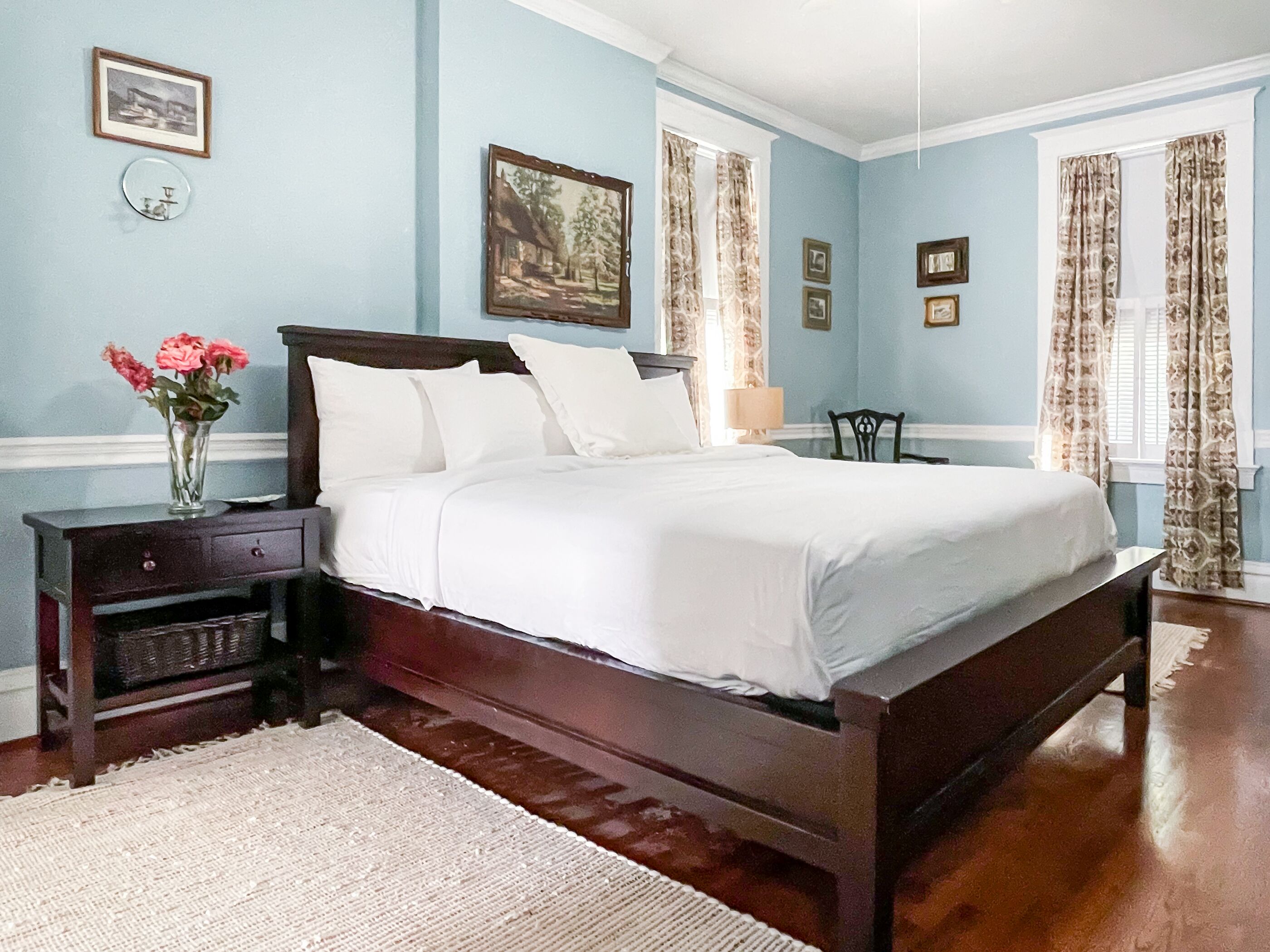 A bedroom with a large bed, a nightstand with a vase of flowers, and a dresser.