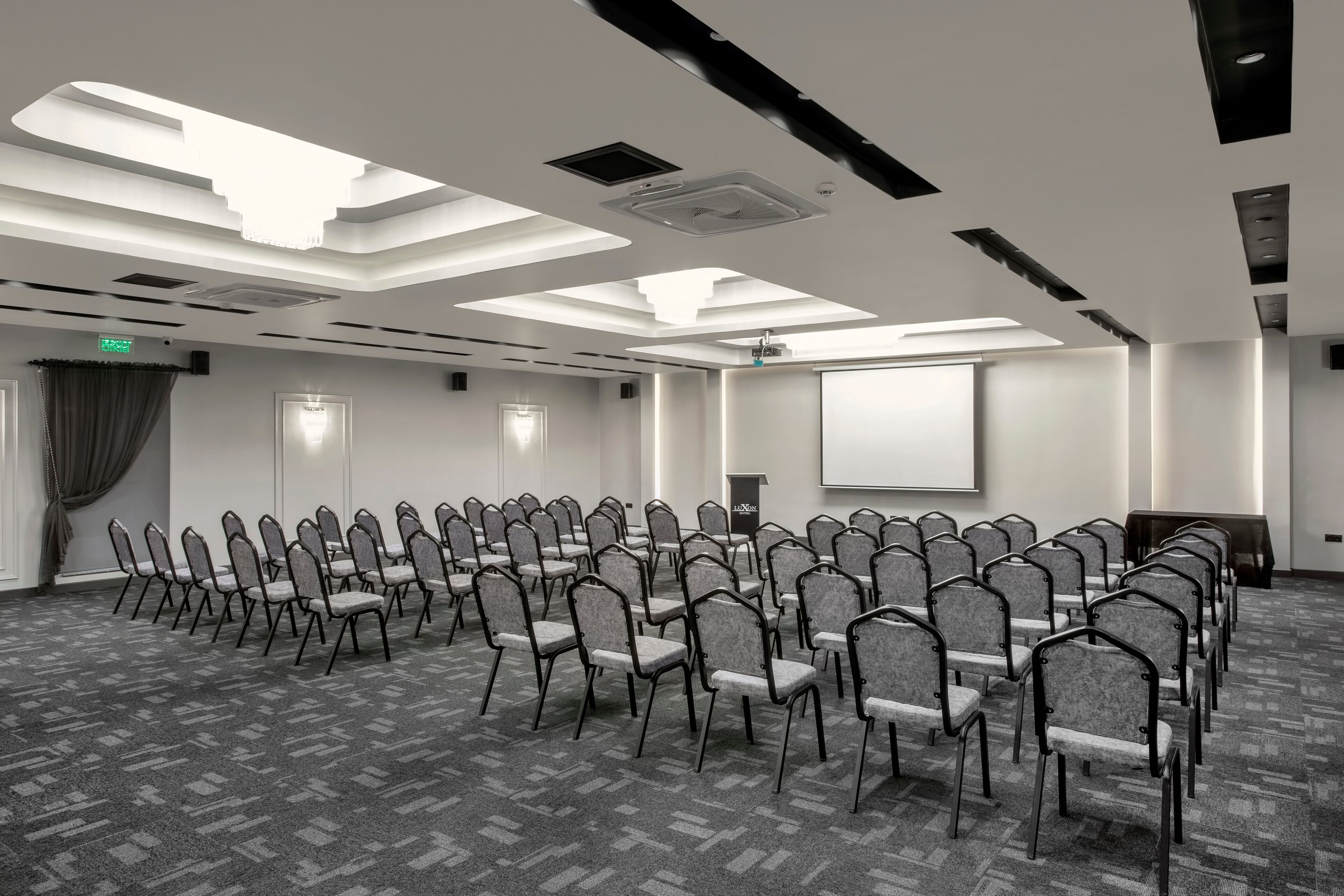 A conference room with rows of chairs, a projector screen, and a ceiling with skylights.
