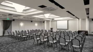 A conference room with rows of chairs, a projector screen, and a ceiling with skylights.