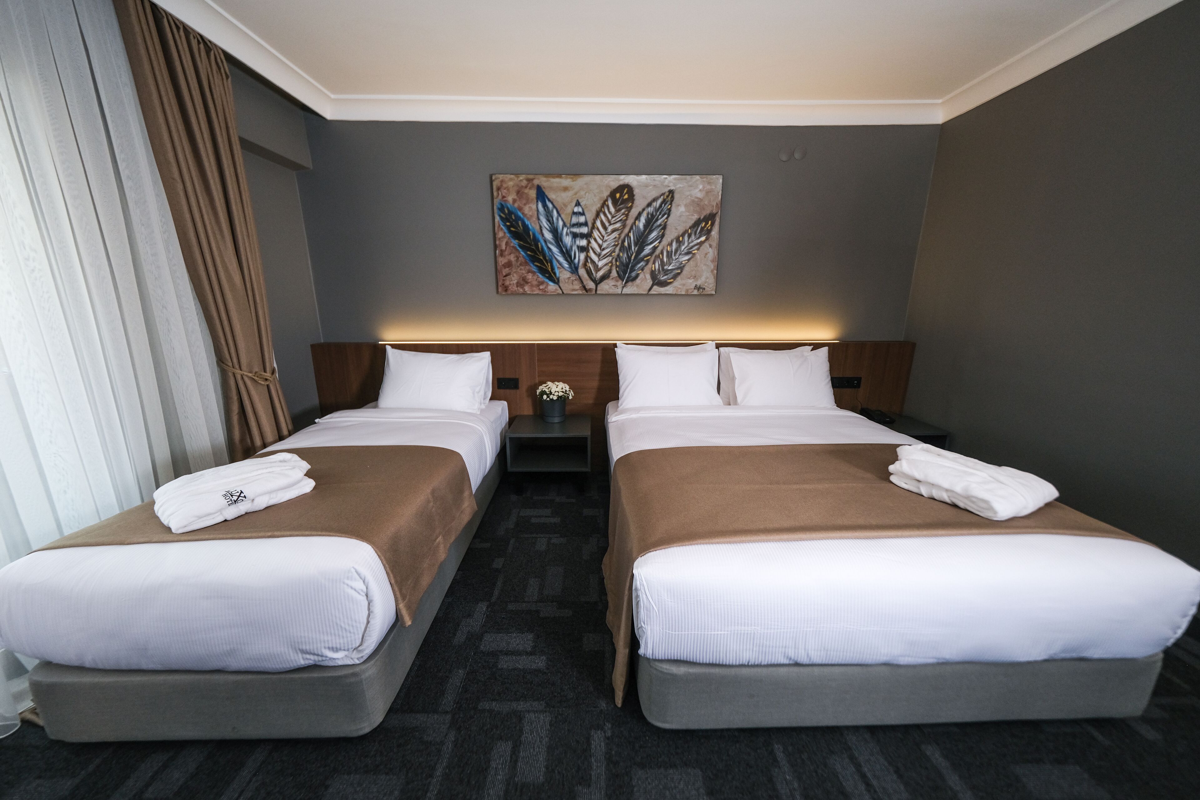 Une chambre d’hôtel avec deux lits, un tableau au mur et une fenêtre avec des rideaux.
