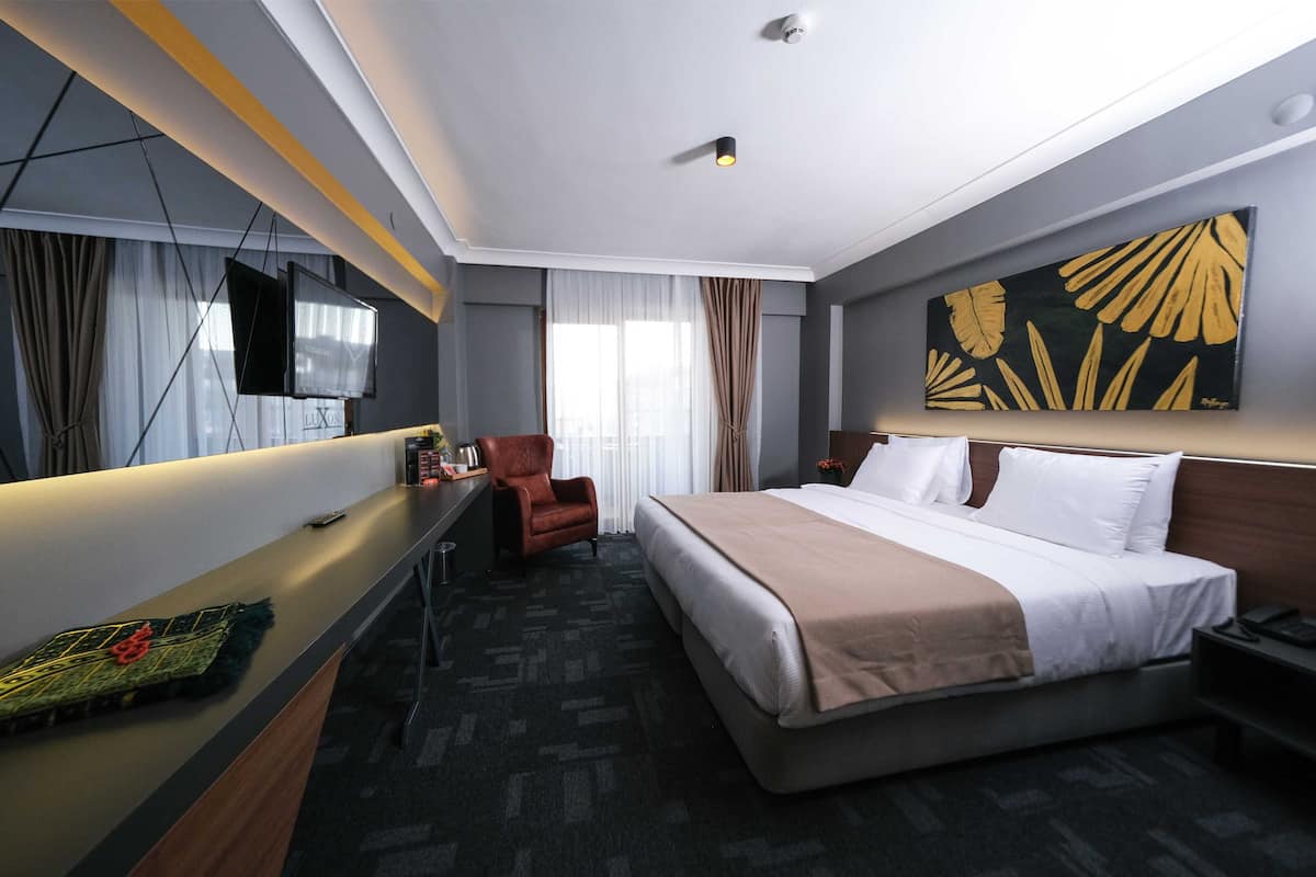 A hotel room with a bed, a desk, a chair, a TV, and a painting on the wall.