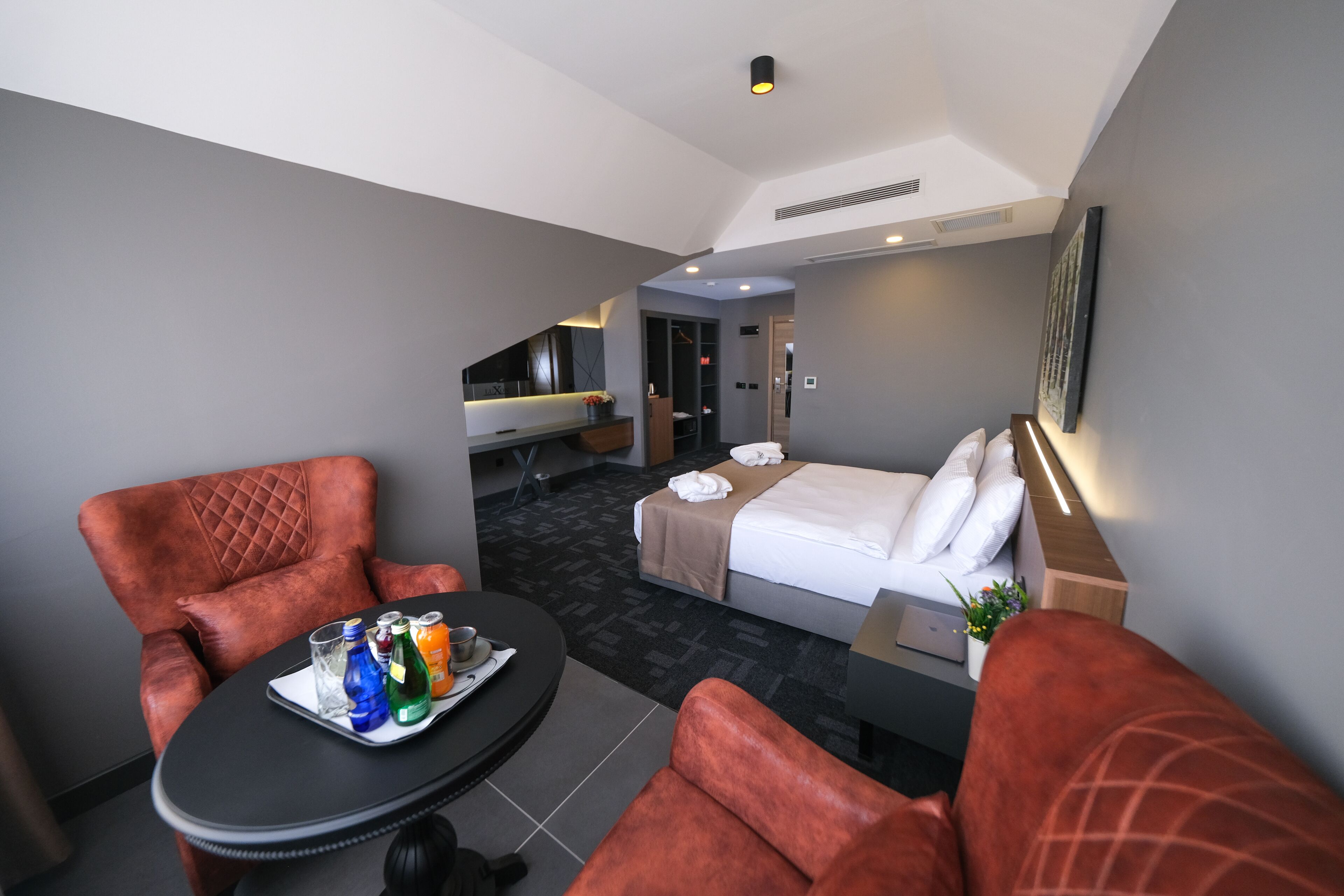 A hotel room with a bed, a desk, a chair, and a small table with drinks and a tray.