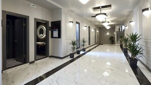 Un pasillo moderno de hotel con suelo de mármol, paredes blanco y negro, y varias puertas que dan a las habitaciones.