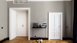 Une pièce avec un parquet en bois disposé en motif de chevron, une porte blanche, un bureau noir avec un ordinateur portable et une petite plante.
