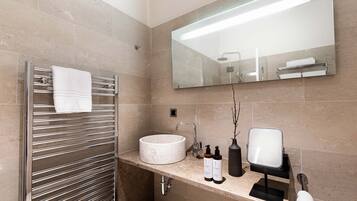 Une salle de bain moderne avec un lavabo rond, un porte-serviettes, un miroir et des articles de toilette disposés sur le comptoir.