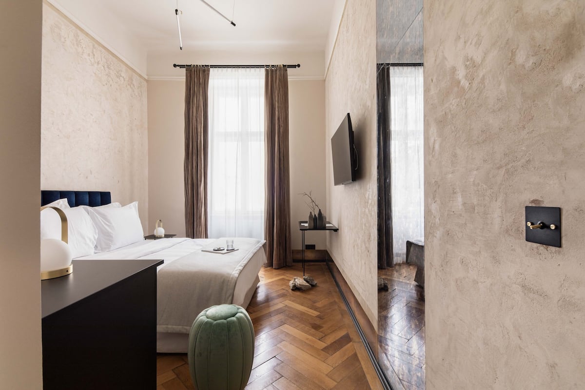 Une chambre d’hôtel moderne équipée d’un lit, d’un bureau, d’un pouf vert, d’un téléviseur à écran plat et d’un mur en pierre.