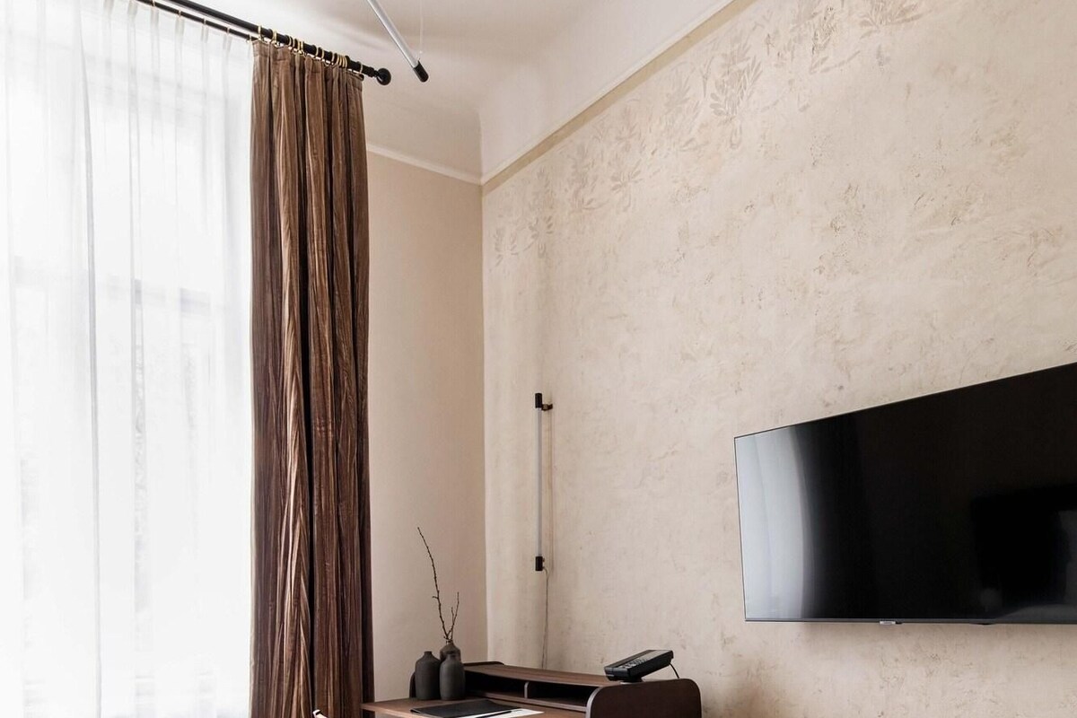 Hotelkamer met een bed, een bureau met stoel, een televisie aan de muur en een raam met gordijnen.