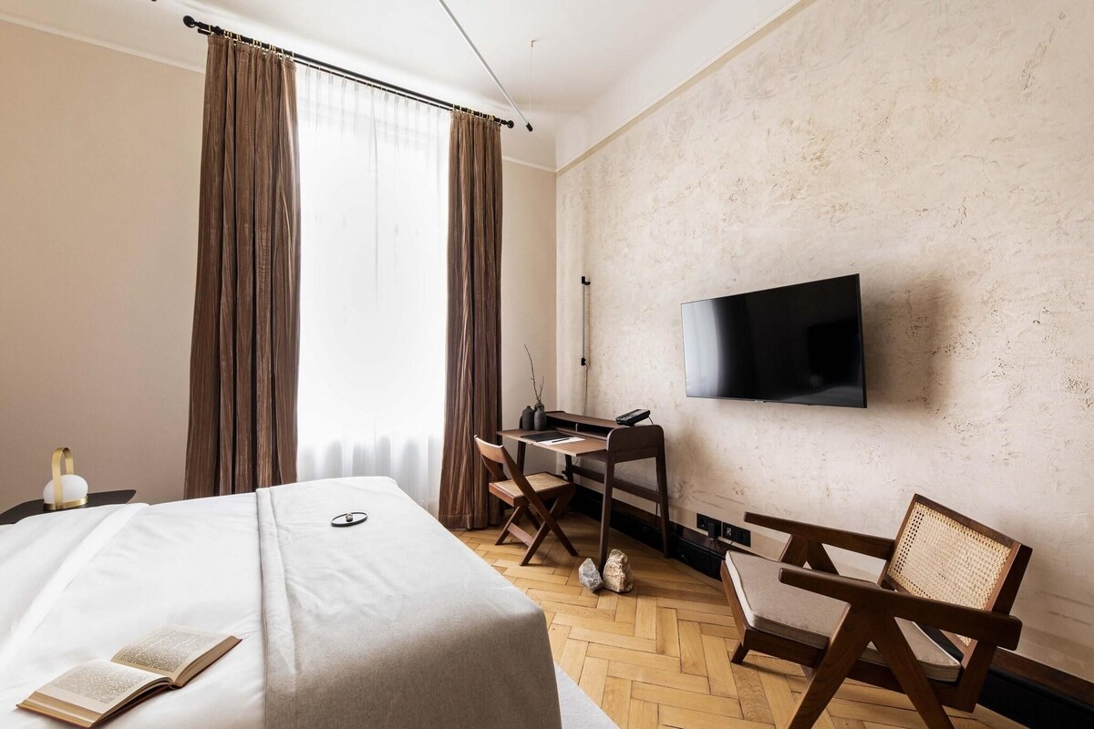 Ein Hotelzimmer mit Bett, Schreibtisch, Stuhl, Fernseher und einem Fenster mit Vorhängen.