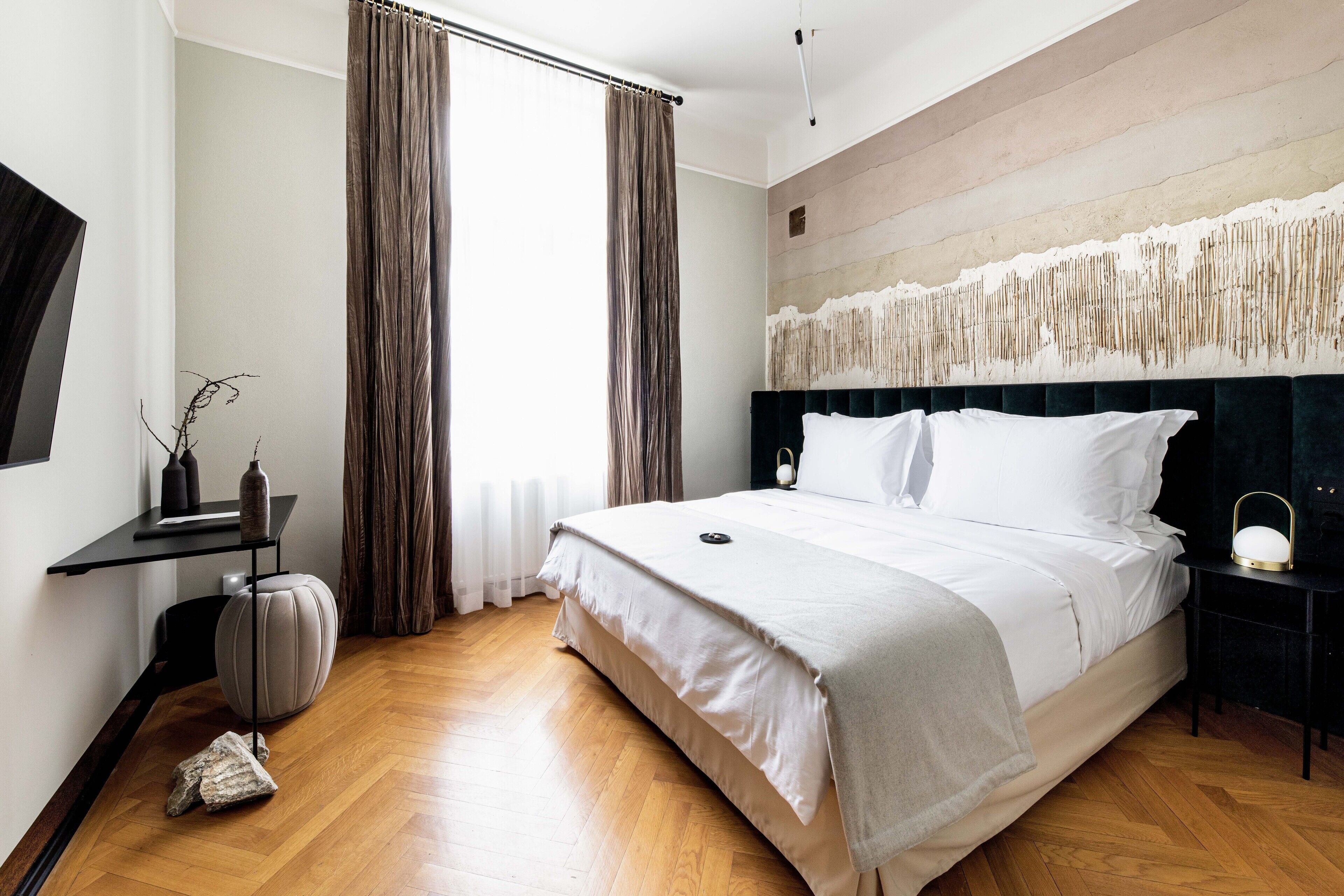 Ein modernes Hotelzimmer mit einem großen Bett, einem Nachttisch, einem Sessel, einem kleinen Tisch und einer Wandleuchte.