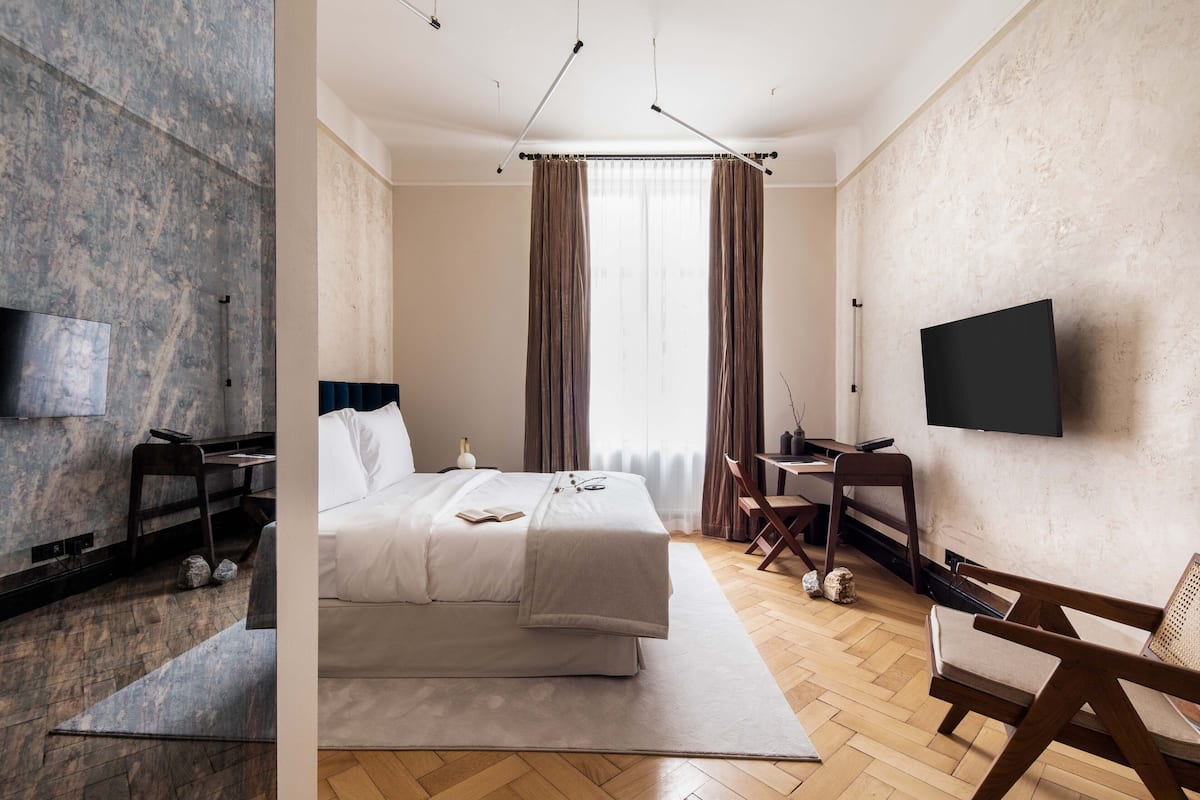 Une chambre d’hôtel moderne équipée d’un grand lit, d’un bureau, d’une chaise et d’un téléviseur à écran plat fixé au mur.