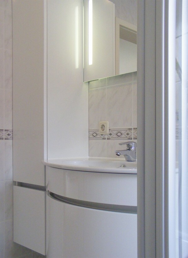 A bathroom with a white sink, a mirror, and a tiled backsplash. - Quiet duplex apartment in Prerow, sleeps 4, parking, Wi-Fi, laundry facilities included. (Ostseebad Prerow)