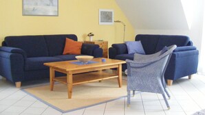 A living room with a blue sofa set, a wooden coffee table, and a striped armchair. - Quietly situated maisonette apartment in Prerow, 4 pers., parking lot, WLAN, laundry incl. (Ostseebad Prerow)