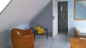 A small, cozy room with a sloped ceiling, a wicker chair, a small table with a yellow decorative item, a wooden bed, and a mirror on the wall. - Quietly situated maisonette apartment in Prerow, 4 pers., parking lot, WLAN, laundry incl. (Ostseebad Prerow)