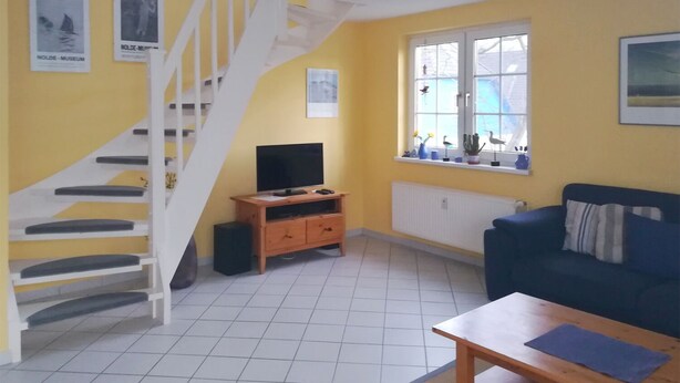 A living room with a staircase, a TV, a sofa, and a window with decorations. - Quietly situated maisonette apartment in Prerow, 4 pers., parking lot, WLAN, laundry incl. (Ostseebad Prerow)