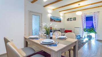 Un comedor con una mesa de madera dispuesta para cuatro personas, un sofá y un ventanal con cortinas.