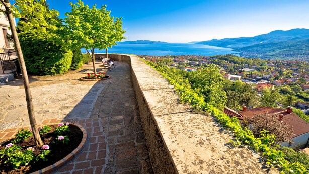 A stone pathway with a bench, surrounded by greenery and a view of a town and water body. - Holiday Home Kastav (Kastav)