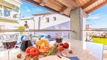Un balcón con una mesa dispuesta para una comida, que incluye una botella, vasos, queso, tomates y frutos secos.