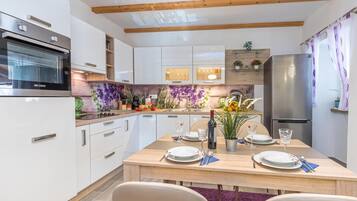 A modern kitchen with white cabinetry, a wooden dining table set for two, and a built-in oven.