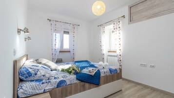 A bedroom with a bed, bedside lamps, a hanging light fixture, and a window with curtains.