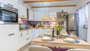 A modern kitchen with white cabinets, a wooden dining table set for four, and a built-in oven. - Holiday Home Kastav (Kastav)