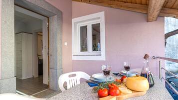 A balcony with a table set for dining, featuring a cheese, tomatoes, and a bottle.