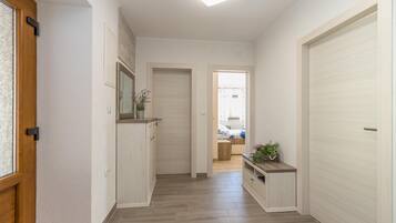 A hallway with wooden flooring, white walls, and a door on the left.