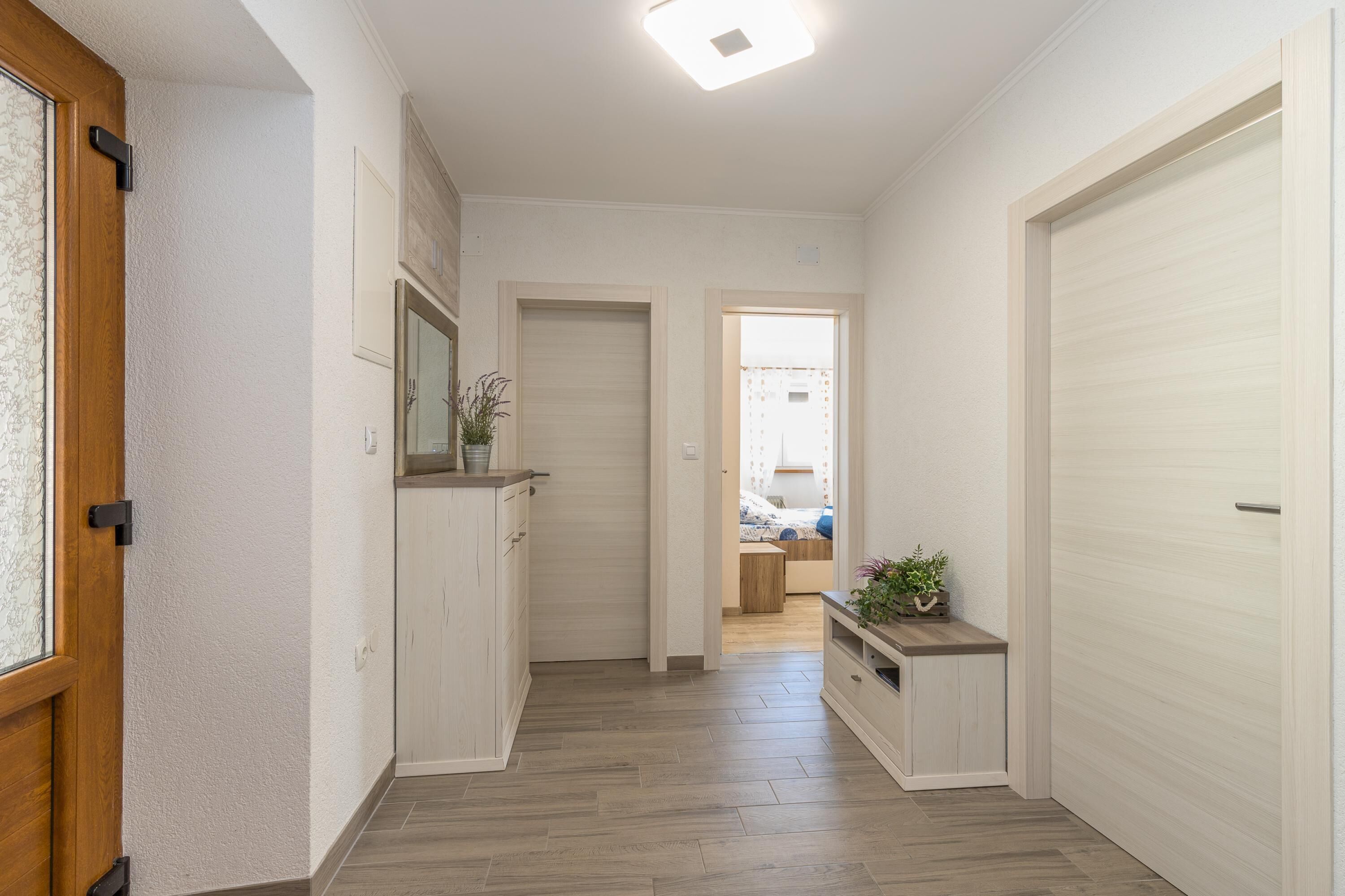 Un couloir avec un plancher en bois, des murs blancs et une porte sur le côté gauche.